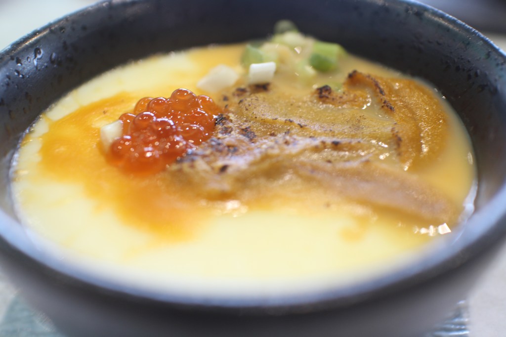 一碗包含鮭魚魚卵和燉蛋的海鮮烘飯,表面撒上切碎的蔥花,內容豐富,呈現出誘人的金黃色。